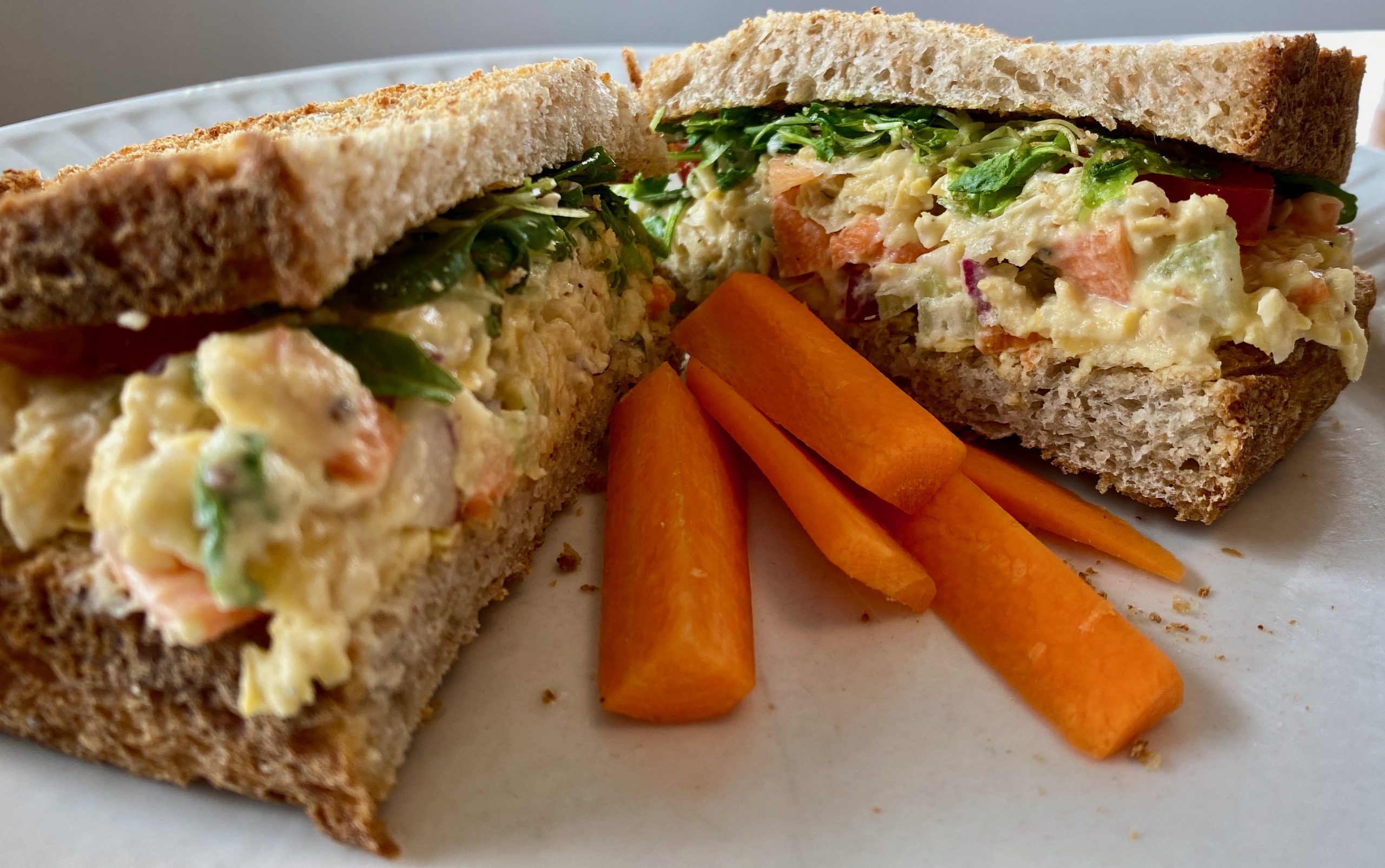 Plated is a sandwich cut in two and set at an open angle. Carrots are placed in between both slices of the sandwich.